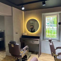 ArMebel - Stylowe wnętrze salonu fryzjerskiego z dwoma fotelami, toaletką z okrągłym lustrem podświetlanym LED i oknem z widokiem na zieleń. Nowoczesny design z elementami retro.
