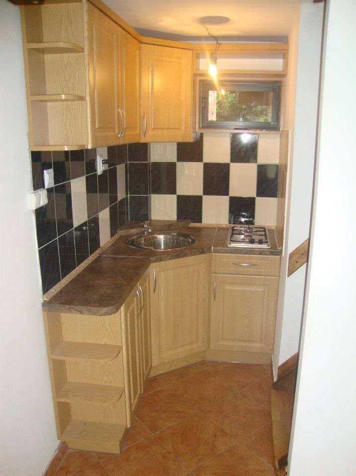 Narożna, jasna zabudowa kuchenna z blatem w odcieniach brązu, czarno-białe płytki nad blatem, mała kuchenka gazowa. Widok na małą, ale funkcjonalną kuchnię.