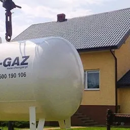 Montaż zbiornika z logo Chem-Gaz na posesji z domem jednorodzinnym, widoczny dźwig i pracownik w tle.