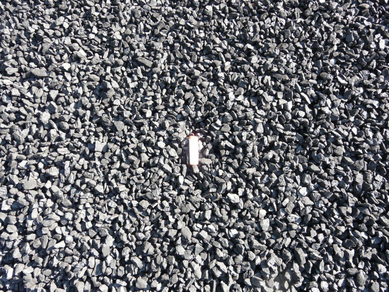 Wysypany na płasko drobny, szary opał węglowy z zapalniczką umieszczoną pośrodku dla skali.