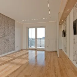 Jasne, przestronne wnętrze po remoncie z drewnianą podłogą, ścianą z szarej cegły, marmurową ścianą z telewizorem i balkonem z widokiem na miasto.