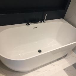 REM-BUDD Piotr Czachowski - Nowoczesna, owalna wanna wolnostojąca z chromowaną armaturą, umieszczona w łazience z czarną wnęką i marmurowymi płytkami.