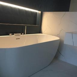 REM-BUDD Piotr Czachowski - Nowoczesna, biała wanna wolnostojąca z chromowaną armaturą na tle ciemnej ściany z podświetleniem LED i marmurowej umywalki w wykończonej łazience w Warszawie.