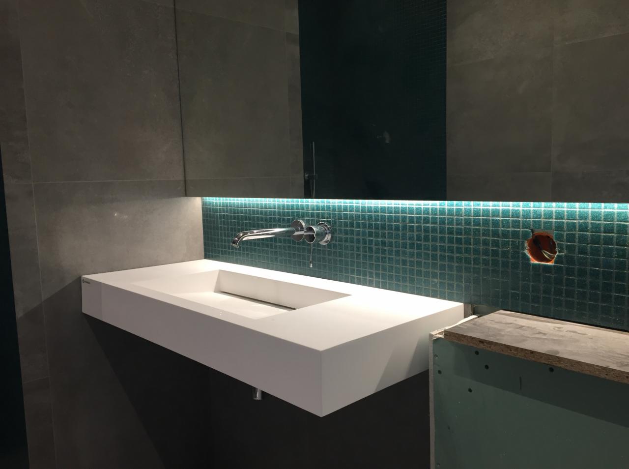 Nowoczesna, prostokątna umywalka nablatowa z chromowaną baterią, podświetlona od dołu zielonymi mozaikowymi płytkami, widoczne przygotowania do montażu gniazdka elektrycznego.