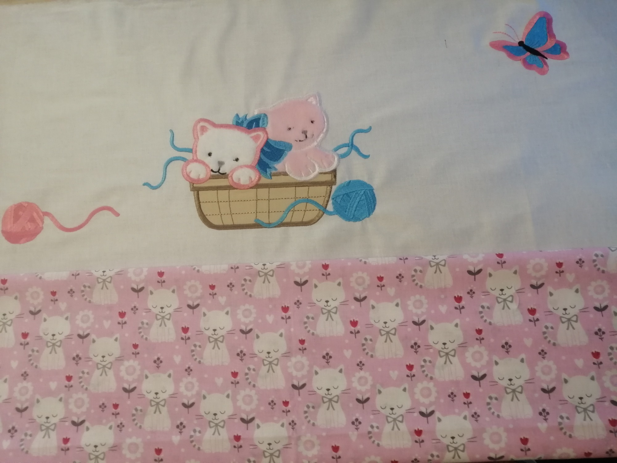 Biała tkanina z haftowanymi kotkami w koszyku i motylem, dolna część z różowym wzorem w kotki i kwiatki.