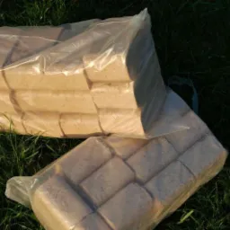 Dwa przezroczyste worki z kostkami drzewnymi RUF leżą na zielonej trawie w słoneczny dzień.