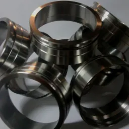 Srebrzyste, metalowe pierścienie z wyżłobieniami, ułożone w nieuporządkowany stos na białym tle, widoczne refleksy światła.