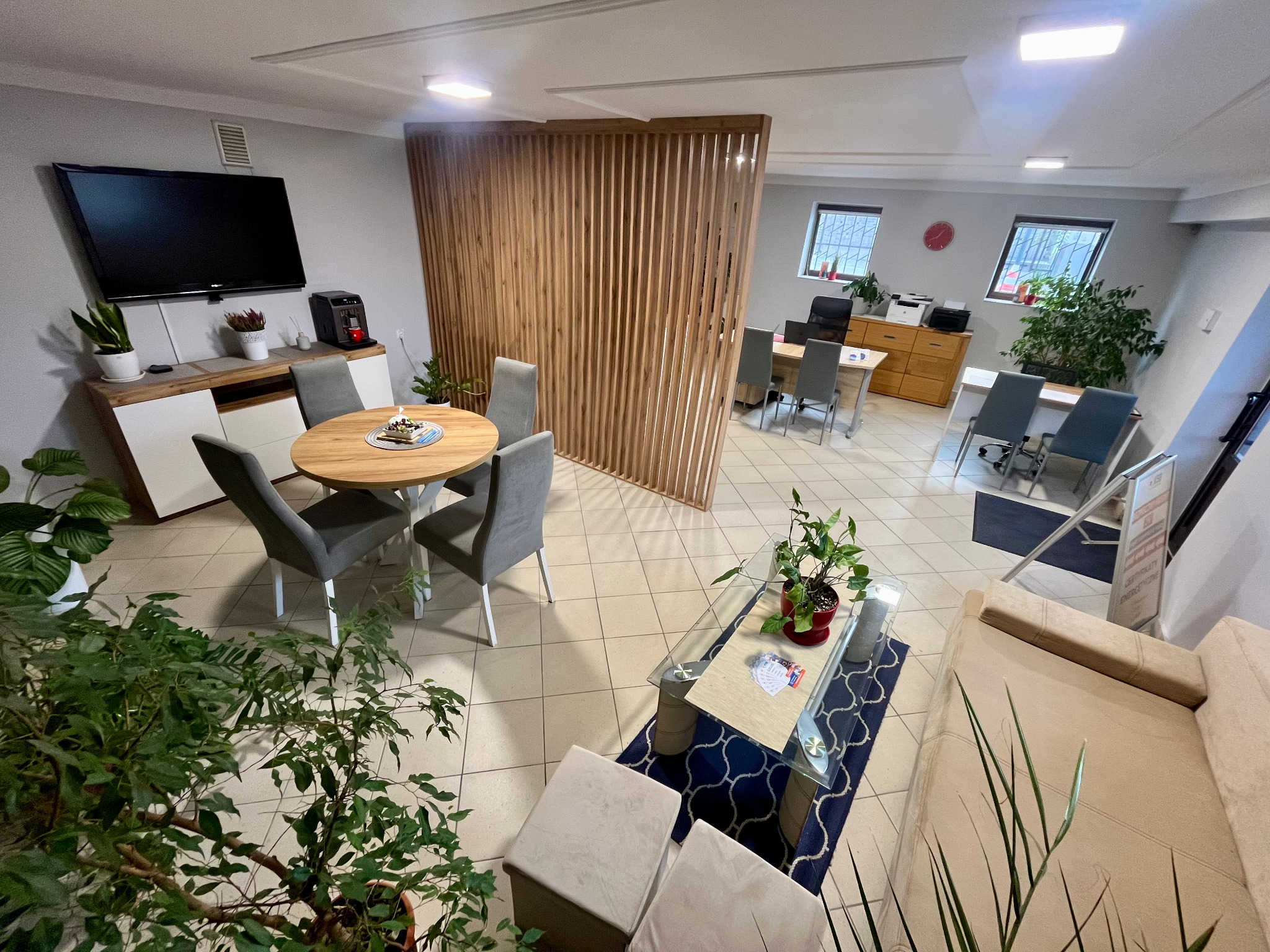 Jasne biuro nieruchomości z drewnianą ścianką działową, okrągłym stołem i roślinami doniczkowymi. Widok z góry na przestrzeń biurową.