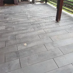 Szara, drewnopodobna podłoga tarasu ułożona z prostokątnych płyt, z widoczną strukturą drewna i zadaszeniem z drewnianą balustradą.