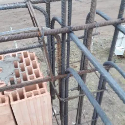 Wiązanie zbrojenia pionowego z poziomym drutem, widoczne bloczki ceramiczne z zaprawą, w tle droga i trawa.