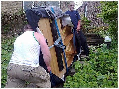 Dwóch mężczyzn w Krakowie przenosi pianino zabezpieczone kocem i pasami po schodach na zewnątrz budynku.