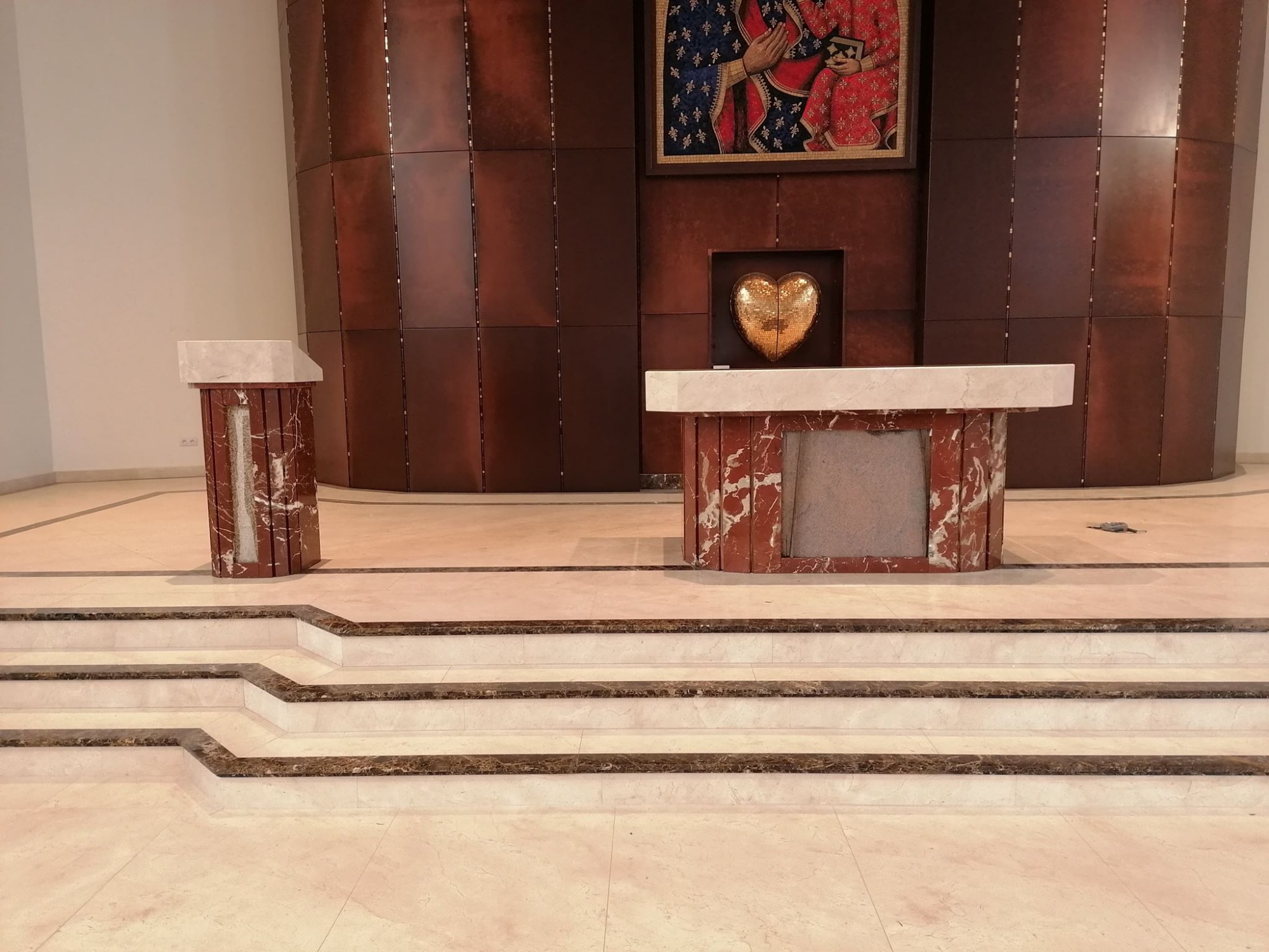 Marmurowe schody prowadzące do ołtarza z marmurowym blatem i podstawą, w tle drewniana ściana z obrazem religijnym i złotym sercem.