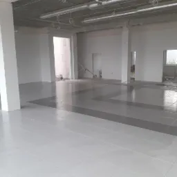 Wykończone podłogi z jasnych i szarych płytek w przestronnym, surowym wnętrzu w Szubinie, widoczne filary i instalacje pod sufitem.