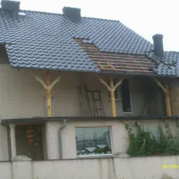 Dom w trakcie naprawy dachu z widoczną więźbą dachową i częściowo ułożonym ciemnym pokryciem