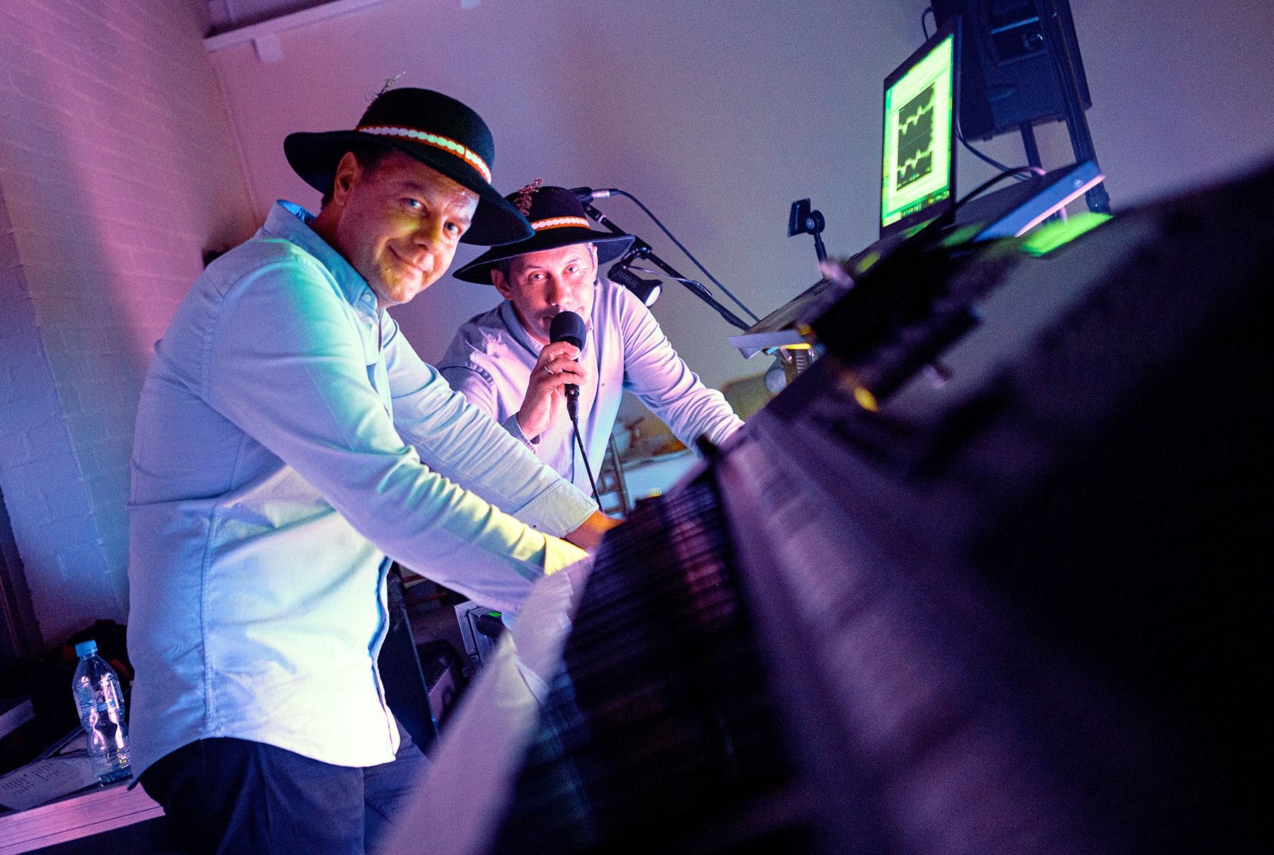 Zespół muzyczny w strojach regionalnych grający na syntezatorze i śpiewający do mikrofonu podczas występu na scenie oświetlonej fioletowym światłem.