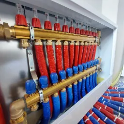 Rozdzielacz ogrzewania podłogowego w szafce, z czerwonymi i niebieskimi rurami, zaworami regulacyjnymi i przepływomierzami, widok z góry