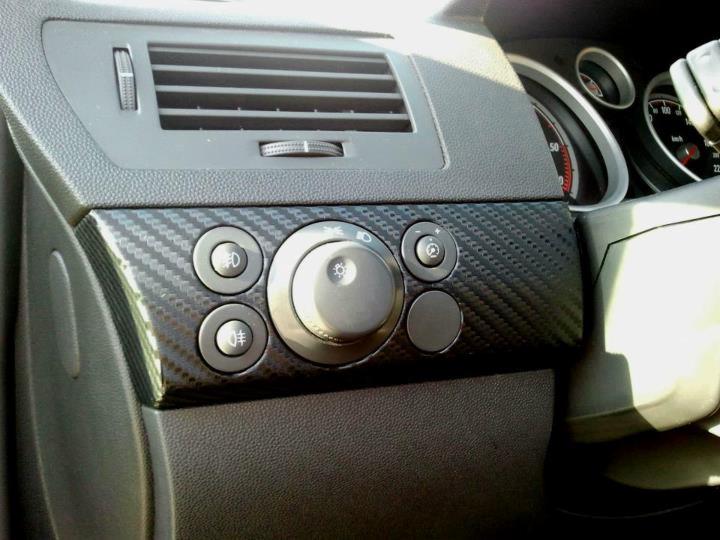 Deska rozdzielcza samochodu z oklejonym panelem sterowania światłami folią imitującą karbon.