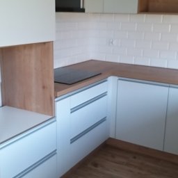 AS Firma Remontowo-Budowlana - Nowoczesna kuchnia z białymi szafkami z poziomymi uchwytami, drewnianym blatem i panelami oraz białymi płytkami typu metro na ścianie, widok z perspektywy podłogi z drewnianymi panelami.