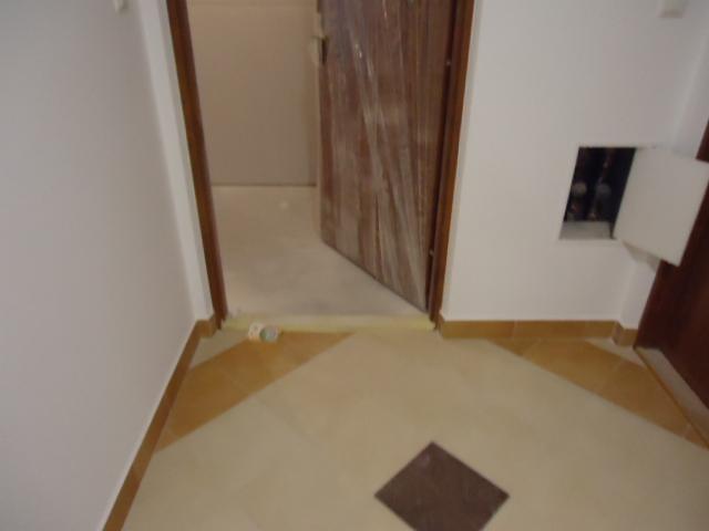 Kafelkowana podłoga w przedpokoju z wzorem geometrycznym, częściowo zakryta folią zabezpieczającą drzwi, widoczna klapka rewizyjna na ścianie.