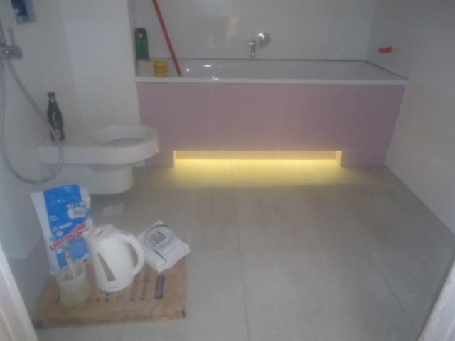 Niedokończony remont łazienki: wanna z podświetleniem, toaleta, płytki podłogowe, opakowanie kleju Ultracolor Plus, czajnik elektryczny i zaprawa na kartonie.