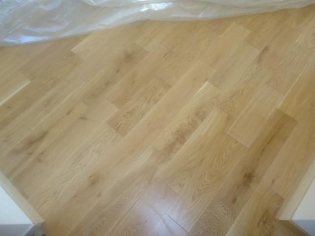 Ułożona w jodełkę jasna, lakierowana podłoga drewniana w trakcie zabezpieczania folią ochronną, realizacja w Warszawie.