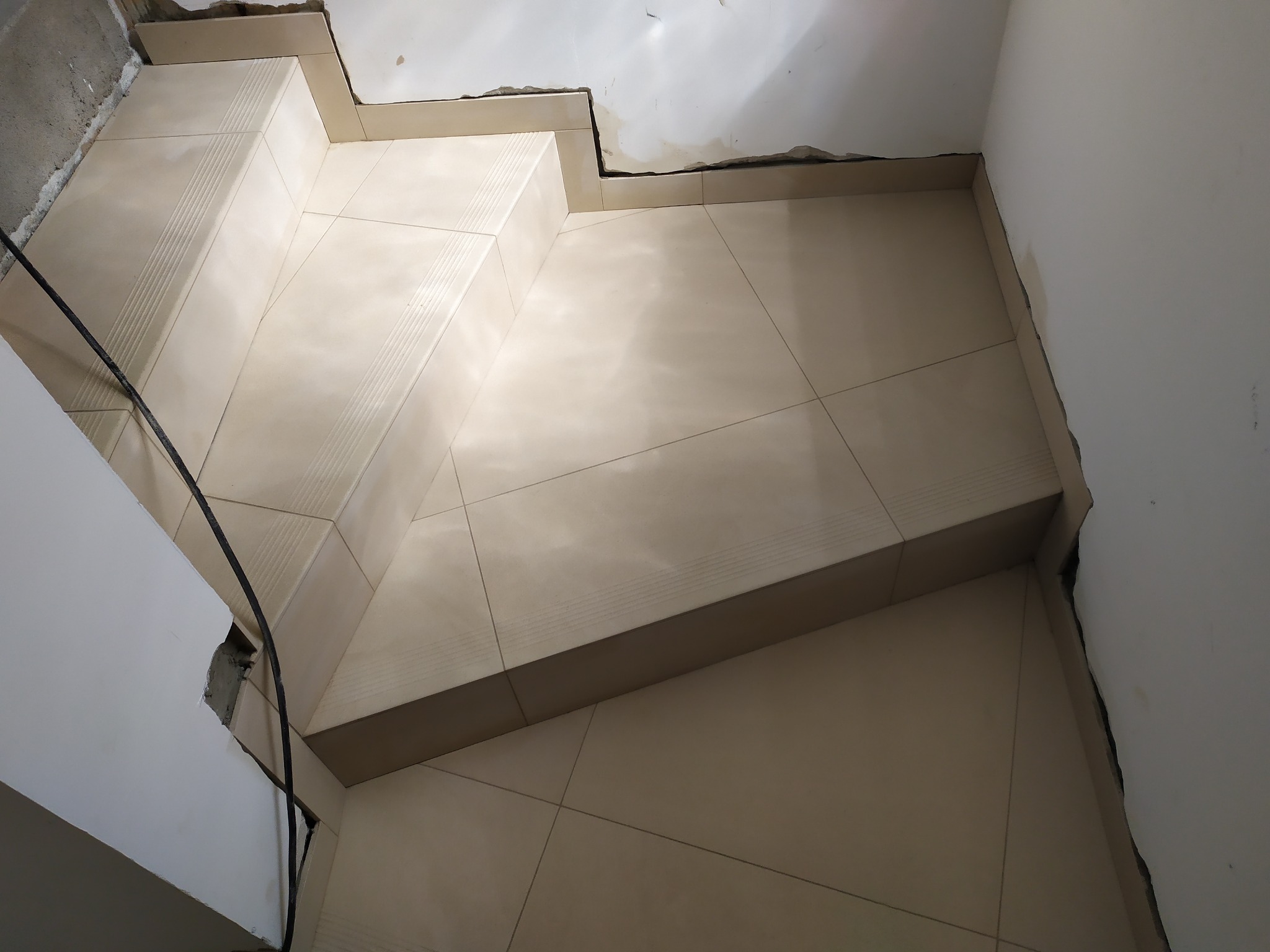 Wyłożone jasnymi płytkami schody w trakcie prac wykończeniowych, widoczne niedoskonałości na ścianach i suficie.