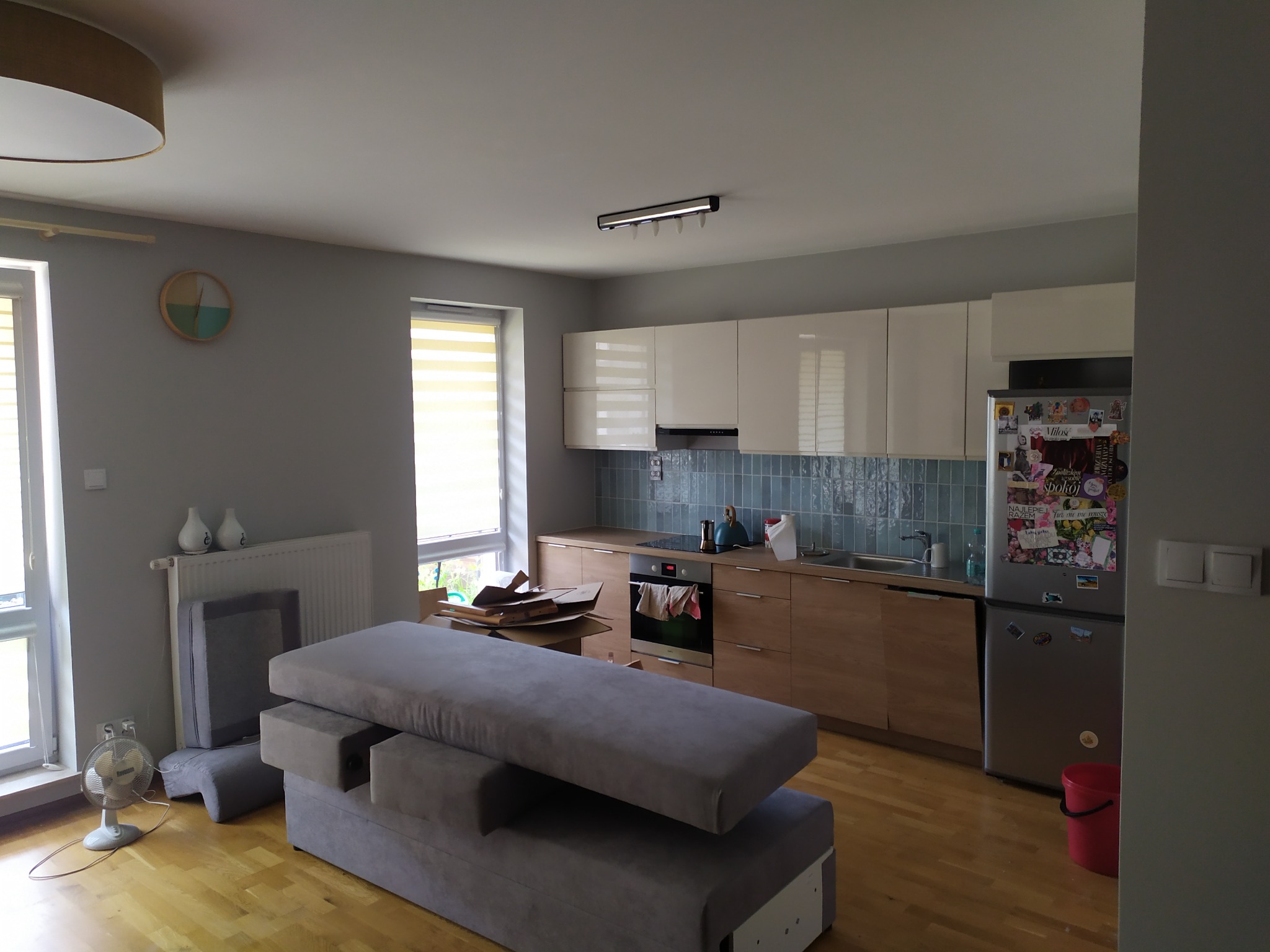 Wnętrze mieszkania w trakcie remontu: widoczny zdemontowany narożnik na parkiecie, w tle kuchnia z zabudową i niebieską glazurą na ścianie.