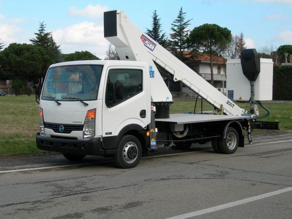 Biały podnośnik koszowy marki GSR 200T na podwoziu samochodu ciężarowego, zaparkowany na poboczu drogi, z widocznym koszem i wysięgnikiem, na tle zieleni i zabudowań.