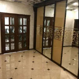 Beżowa, błyszcząca podłoga z ciemnymi wstawkami, duże, przesuwne drzwi z lustrami i dekoracyjnym wzorem, dwuskrzydłowe drzwi z szybami, dekoracyjny sufit w wykończonym wnętrzu.