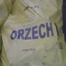 Żółty worek 25 kg z węglem orzech marki Ferbon, widoczne oznaczenia LDPE. W tle inne worki, ciemne tło. Lekki kąt z góry.