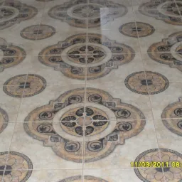 Beżowe płytki podłogowe z ornamentami w kształcie kwiatów i meandrów, ułożone w symetryczny wzór.