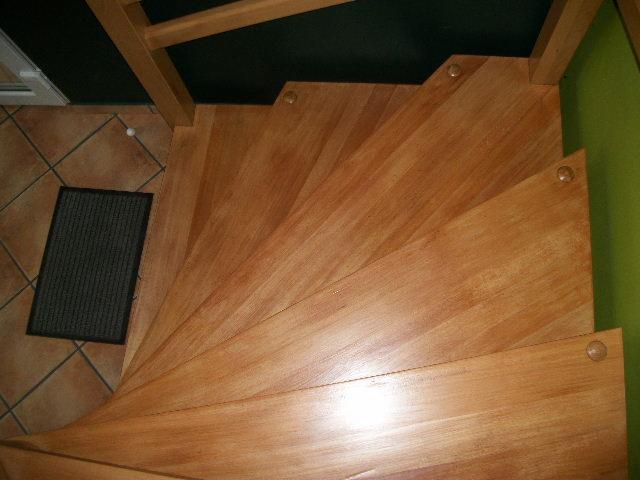 Drewniane, spiralne schody po renowacji, widok z góry, z widocznymi detalami wykończenia i fragmentem płytek na podłodze.