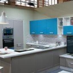 Sklep Meblowy - Nowoczesna kuchnia w loftowym stylu z szarymi szafkami dolnymi i turkusowymi górnymi, wyspą z blatem roboczym, białym oświetleniem punktowym i telewizorem na szafce pod telewizor.