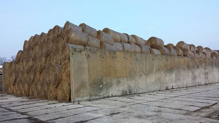 Stos balotów słomy żytniej ułożonych za betonowym murem, na betonowym placu, widok z dołu, pochmurne niebo w tle.