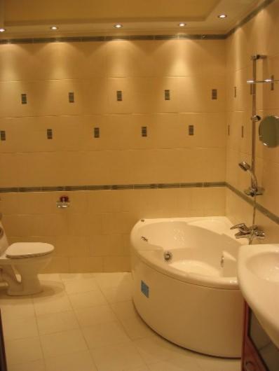 Jasna łazienka z beżowymi płytkami, narożną wanną z hydromasażem, toaletą i chromowaną armaturą.