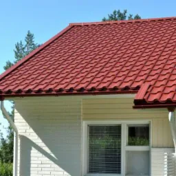 Czerwona blachodachówka Adamante Plus na dachu domu jednorodzinnego z białymi ścianami i oknem.