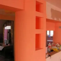 Pomarańczowa ściana z trzema wnękami, fragment sufitu i przejścia do innego pomieszczenia. Ściana częściowo zagruntowana. Widok z perspektywy.