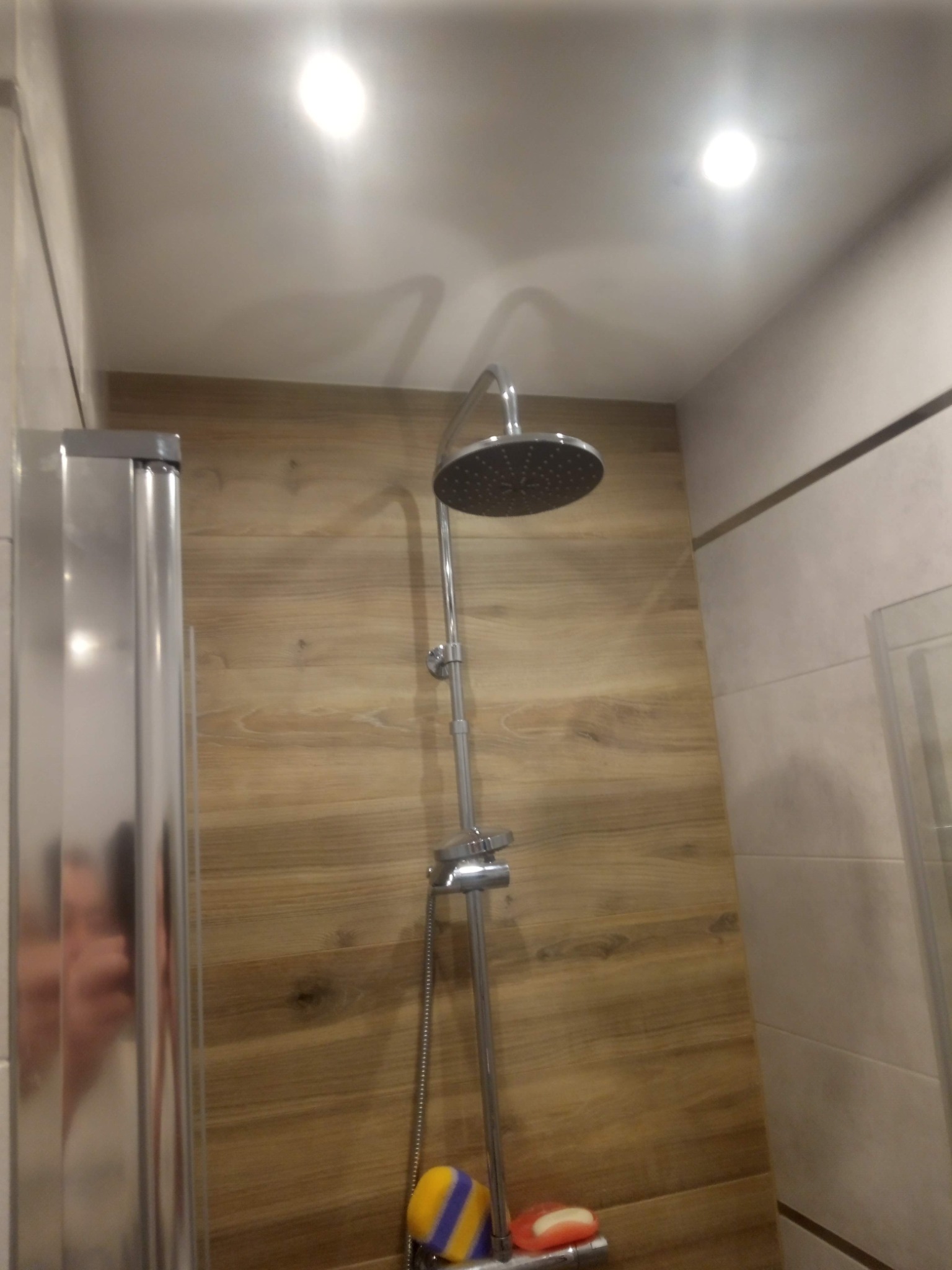 Kabina prysznicowa z deszczownicą i drewnopodobnymi płytkami w Płocku. Widoczna myjka i mydło. Nowoczesne wykończenie łazienki.