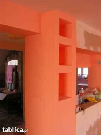 Pomarańczowa ściana z trzema wnękami, fragment sufitu i przejścia do innego pomieszczenia. Ściana częściowo zagruntowana. Widok z perspektywy.