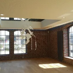 Wnętrze loftu z ceglanymi ścianami, drewnianą podłogą i oświetleniem LED w suficie, podkreślającym industrialny charakter, widoczne okna szprosowe i grzejnik panelowy.