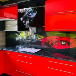 Czerwone szafki kuchenne z czarnym blatem i panelem szklanym z motywem róży, widoczne naczynia i akcesoria kuchenne.