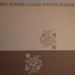 Ściana z dwoma pasami kolorów rozdzielonymi poziomą linią, ozdobiona dekoracyjnymi, kwiatowymi wzorami szablonowymi i bordiurą pod sufitem.