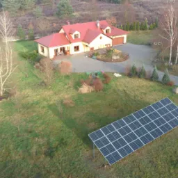 Panel słoneczny na trawniku przed domem jednorodzinnym z czerwonym dachem, widok z góry, jesienna sceneria.