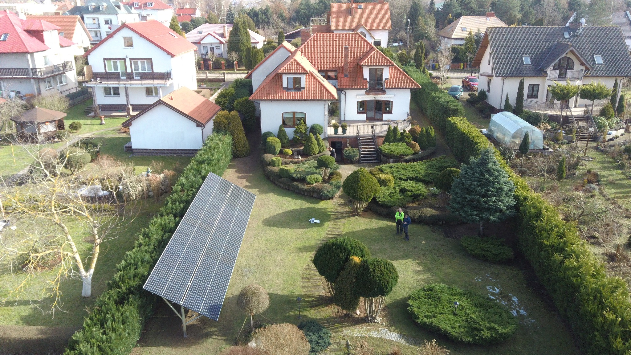 Widok z góry na dom jednorodzinny z ogrodem, na trawniku zamontowany panel słoneczny, obok panelu dwóch mężczyzn w odblaskowych kamizelkach.