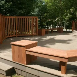 Przestronny taras z kompozytowych desek z drewnianą zabudową: ławki, donice i zaokrąglone, pionowe ogrodzenie, otoczony zielenią.