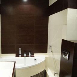 OPTIMA Sebastian Dudek - Nowoczesna łazienka z wanną narożną obłożoną mozaiką, brązowymi płytkami imitującymi drewno na ścianie i podwieszaną toaletą.