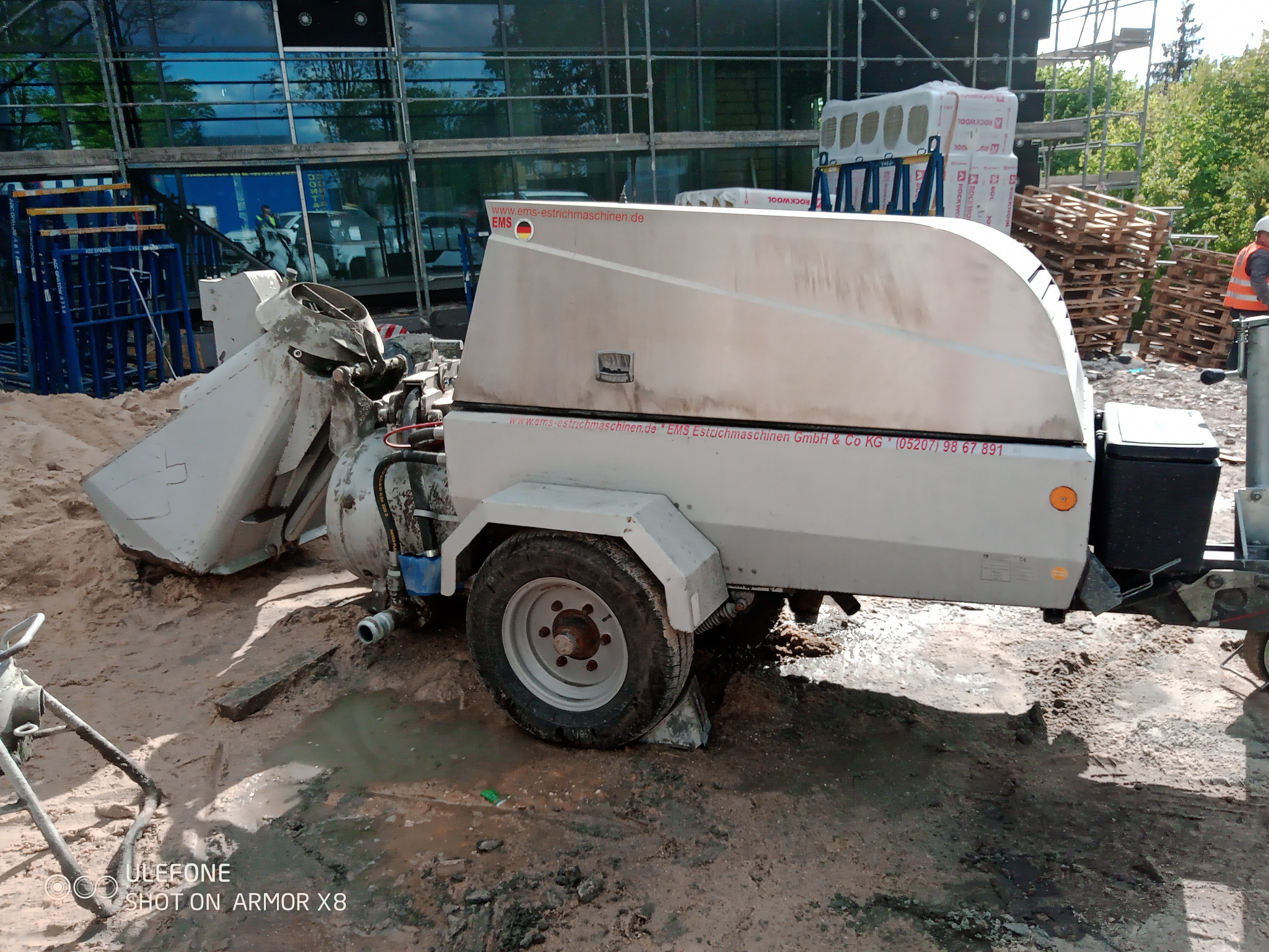 Mobilna pompa do wylewek z widocznym logo producenta EMS Estrichmaschinen, ustawiona na placu budowy z materiałami izolacyjnymi w tle.