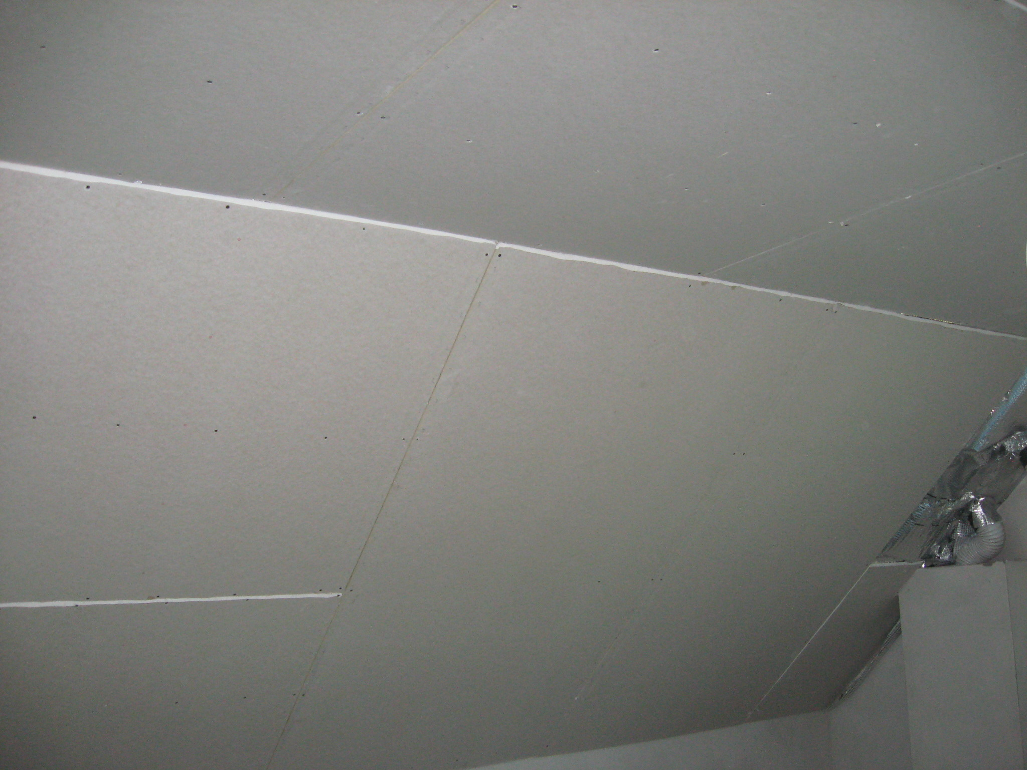 Płyty gipsowo-kartonowe zamontowane na poddaszu, widoczne łączenia płyt i elementy instalacji wentylacyjnej.