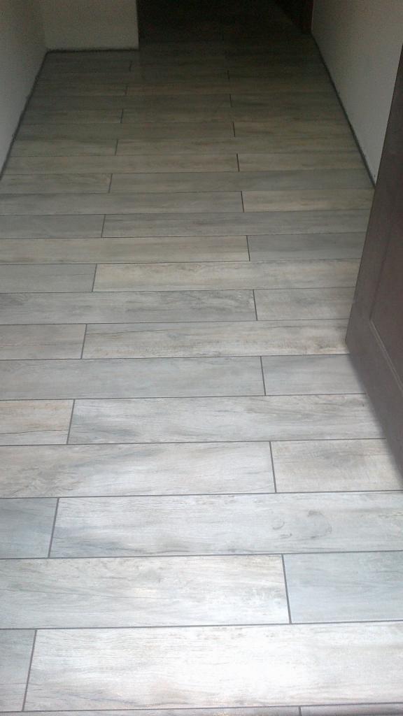 Ułożona podłoga z płytek imitujących drewno w Radlinie. Jasne, podłużne płytki z szarą fugą prowadzą do ciemniejszego pomieszczenia w głębi.