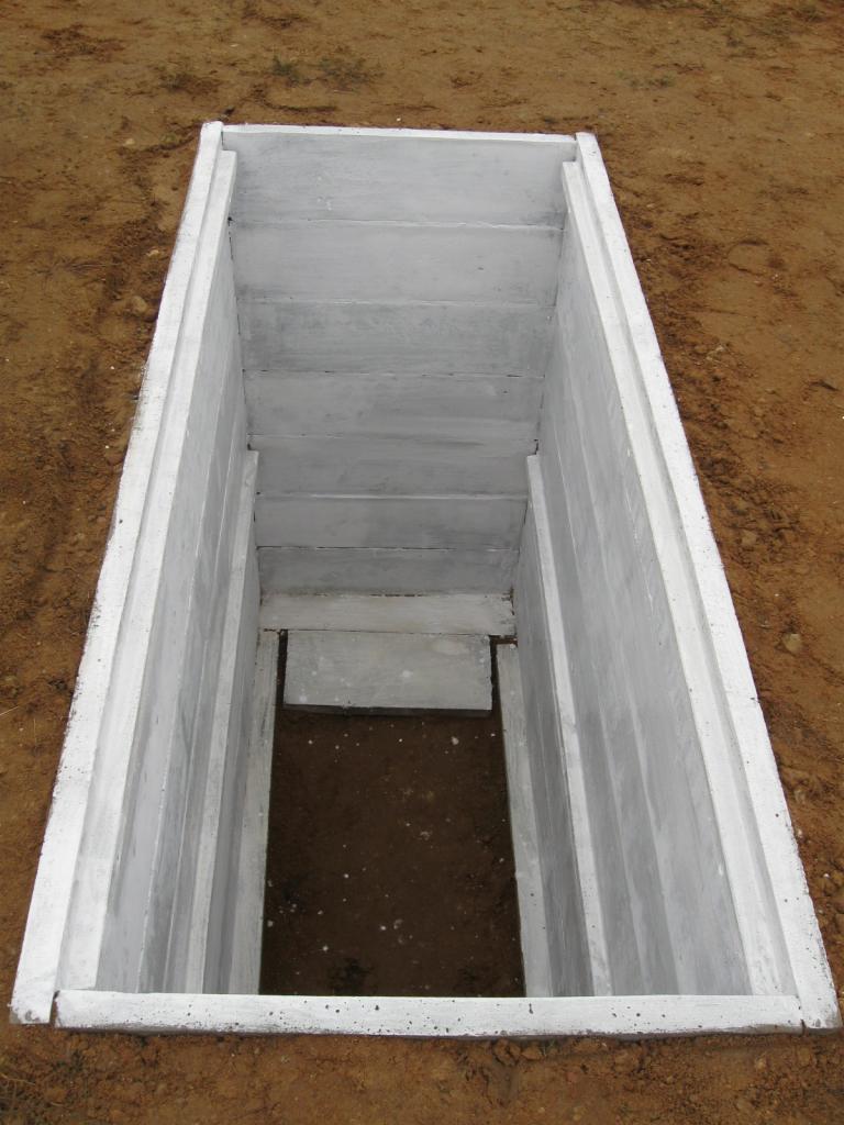 Otwarty prefabrykowany element betonowy, prawdopodobnie piwnica cmentarna, umieszczony w wykopie ziemnym, widok z góry.